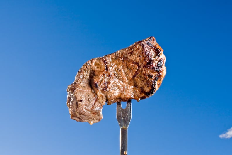 A grilled steak on a fork against a blue sky